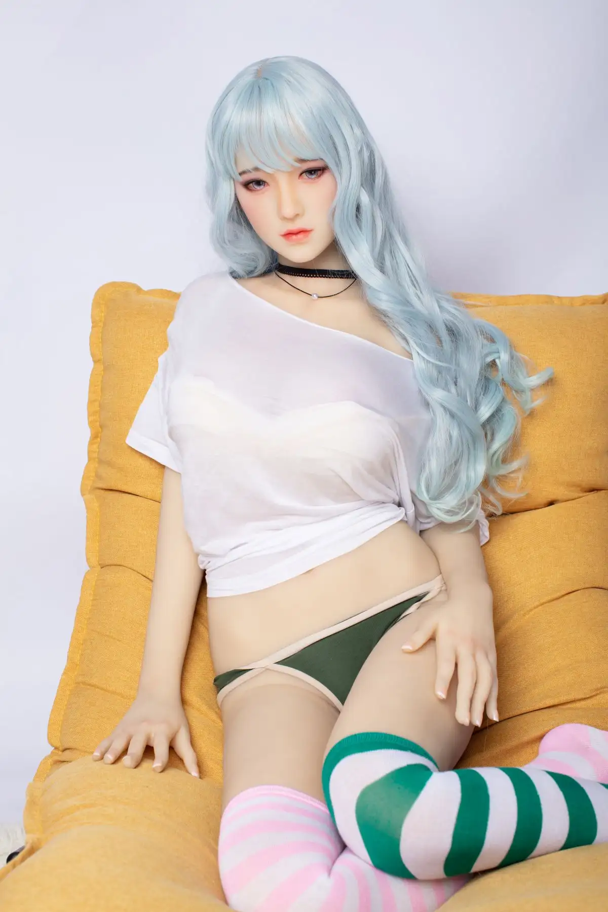 A Japanese style d-cup super realistic tpe sex doll leads against a yellow sofa, wearing a white T-shirt and over-the-knee socks.