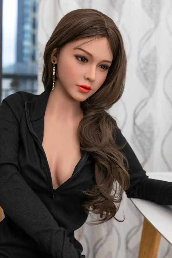 A sex doll in long black sleeves with her hair turned to the side and her hands resting on a table.