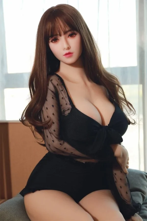 A sex doll with long hair and bangs sat on a couch, her right hand touching her left elbow.