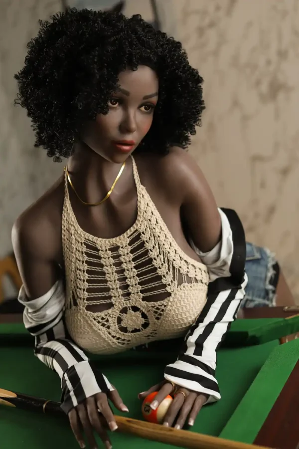 A black afro sex doll wearing an apricot halter is leaning over a pool table.