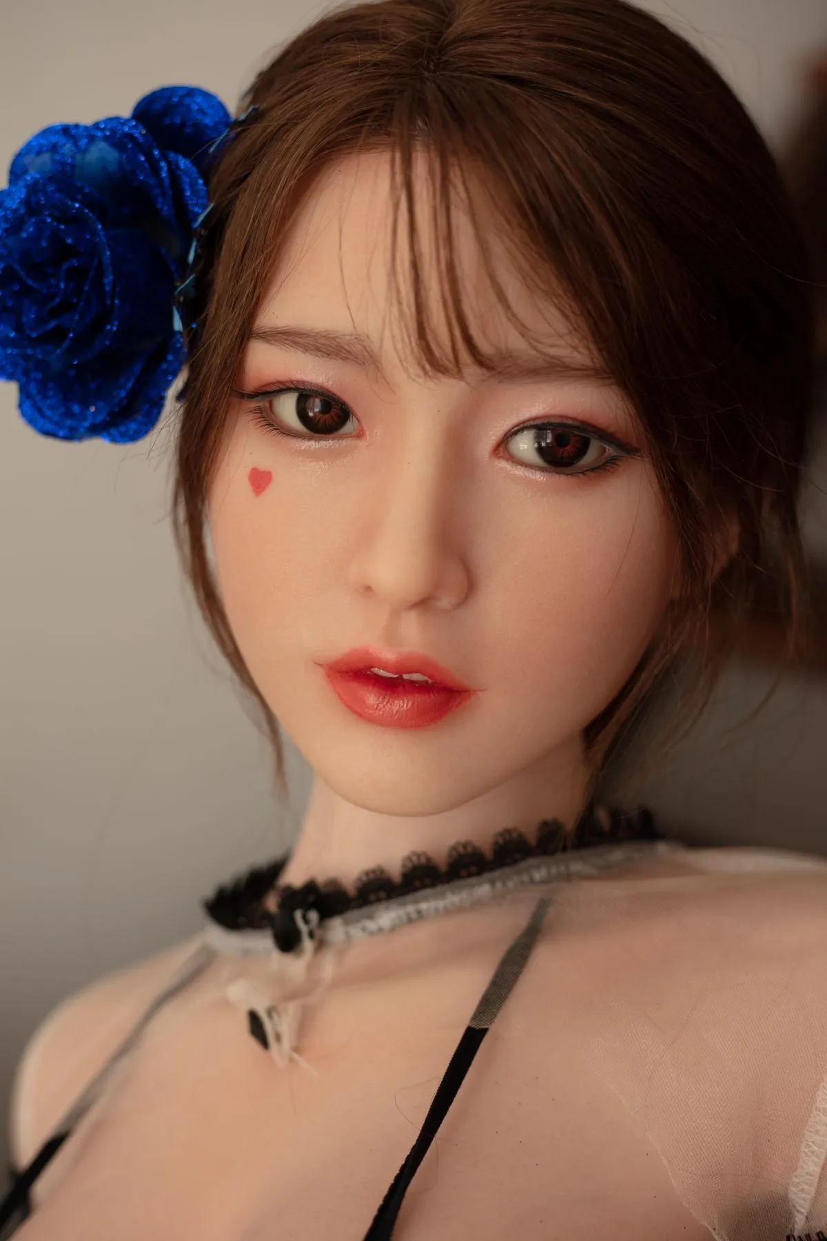 A sex doll with a blue fleece on her head, heart makeup on her face, and a collarbone chain.