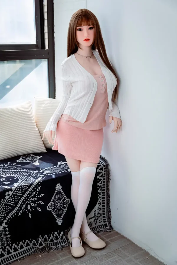 A Japanese sex doll leans against a wall, legs folded, showing off her graceful curves.