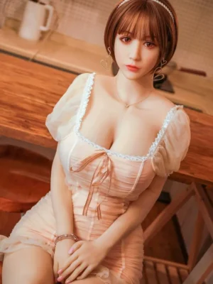 A cute young sex doll in a pink square-necked dress sits on a chair with her hands between her legs.